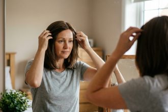 Femme atteinte de cancer essayant une perruque brune devant son miroir dans sa chambre